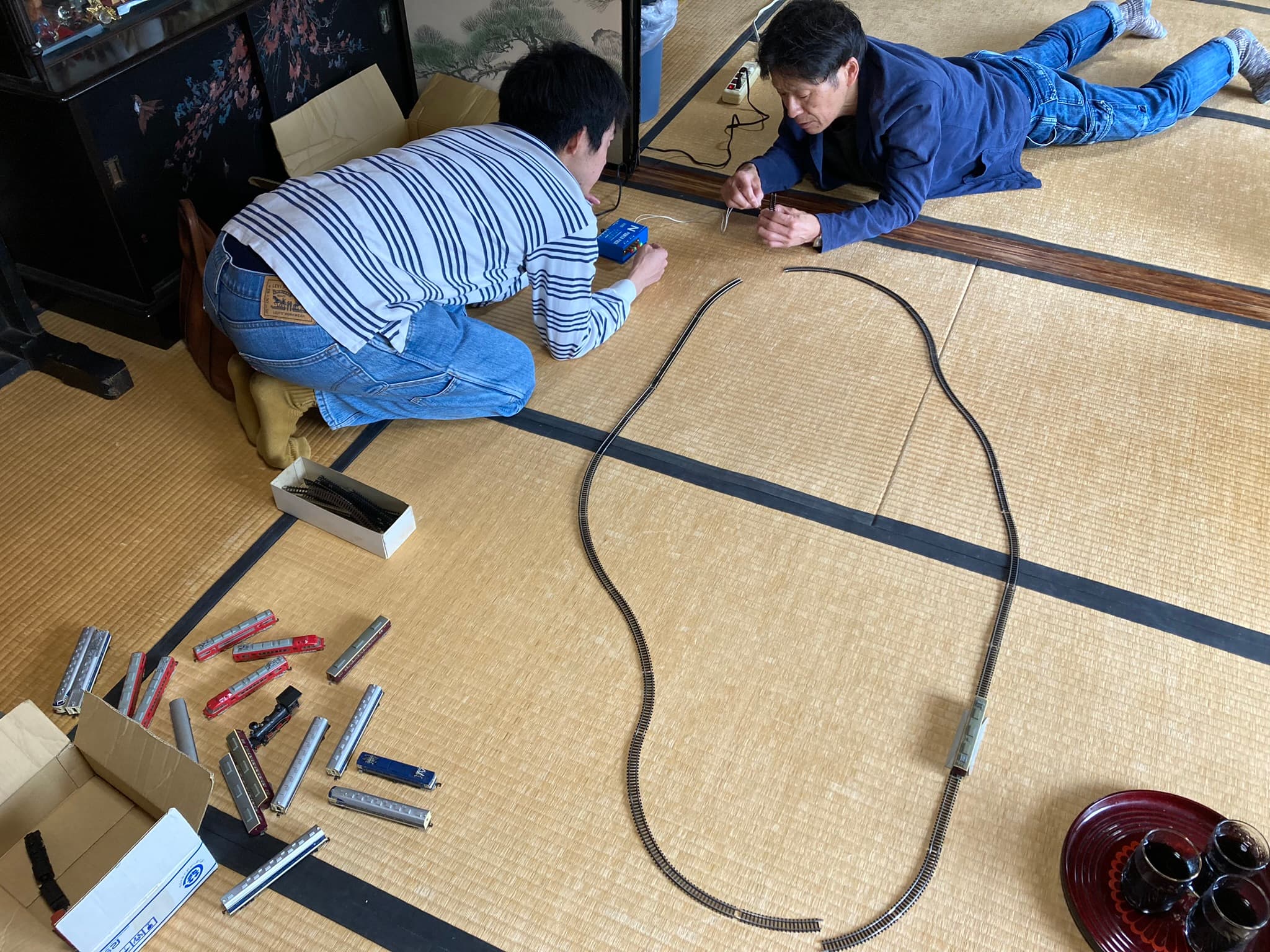 畳の部屋で大人と子どもが一緒にプラレールで遊ぶ様子